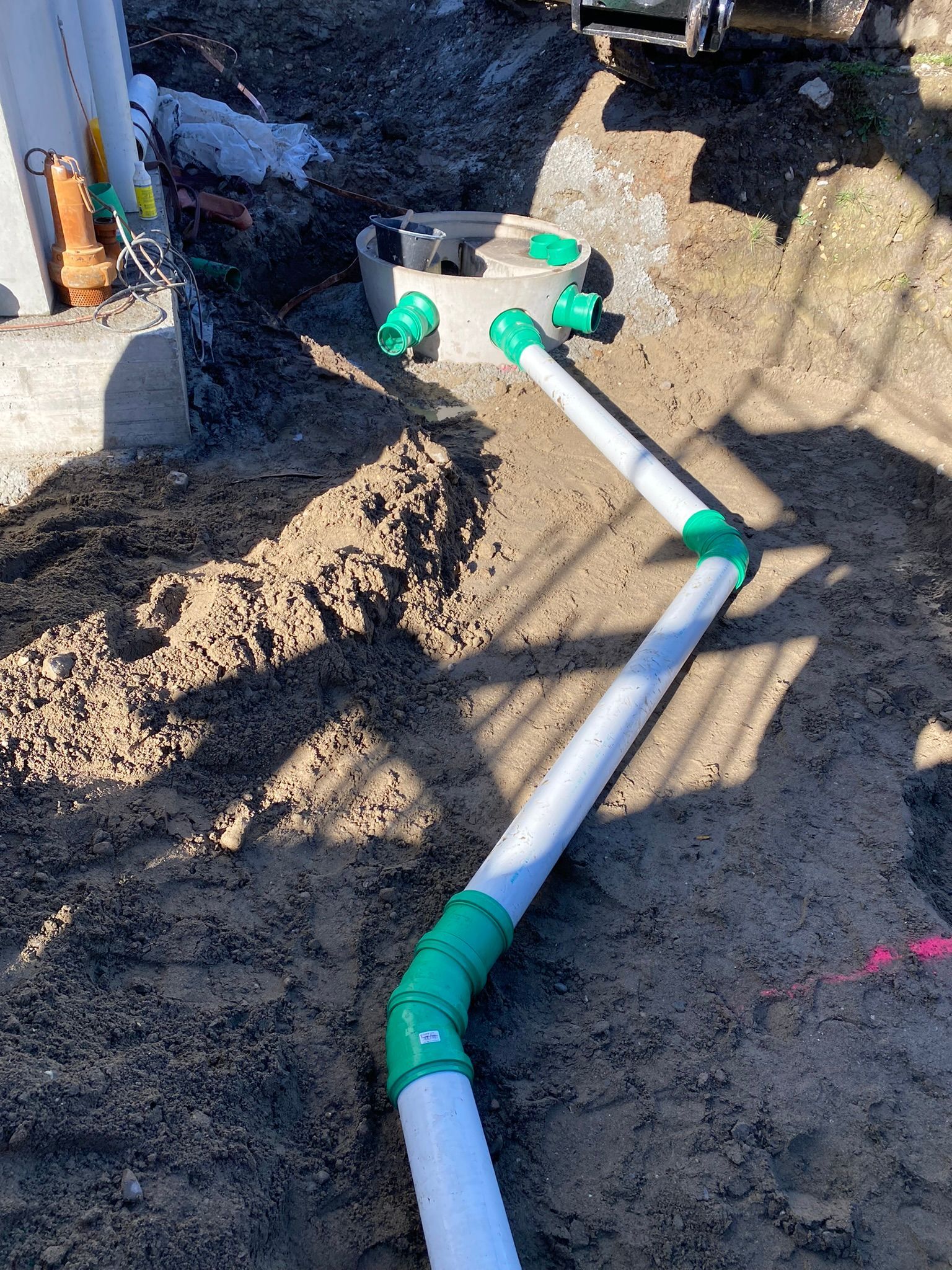 Ein weißes Rohr mit grünen Anschlüssen liegt im Dreck.