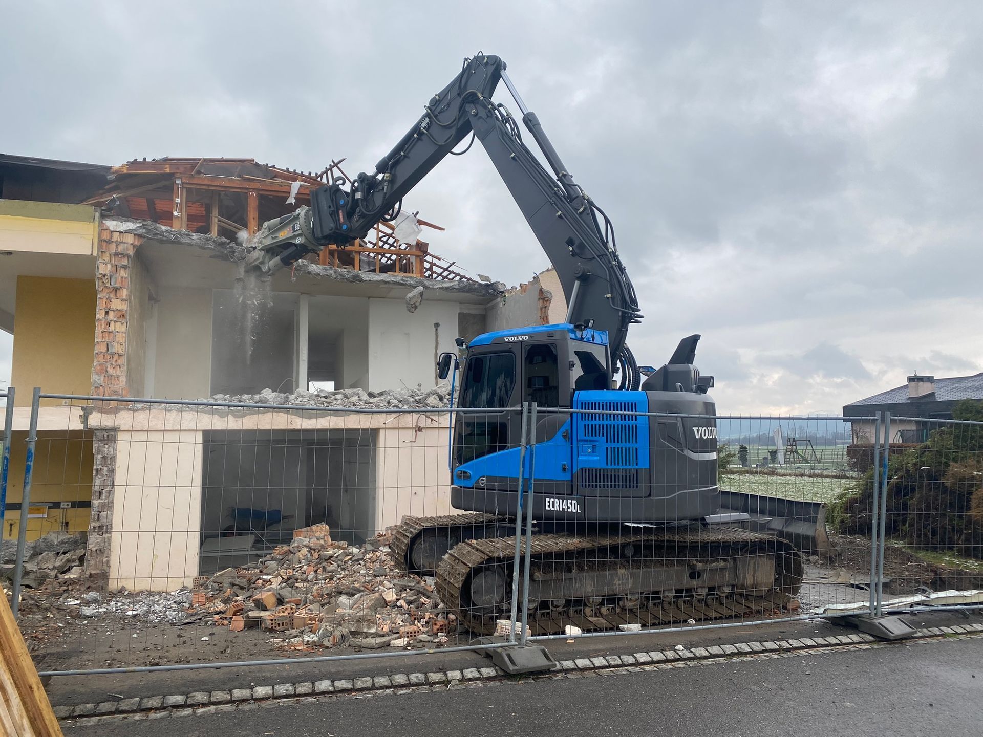 Ein blau-schwarzer Bagger zerstört ein Gebäude.