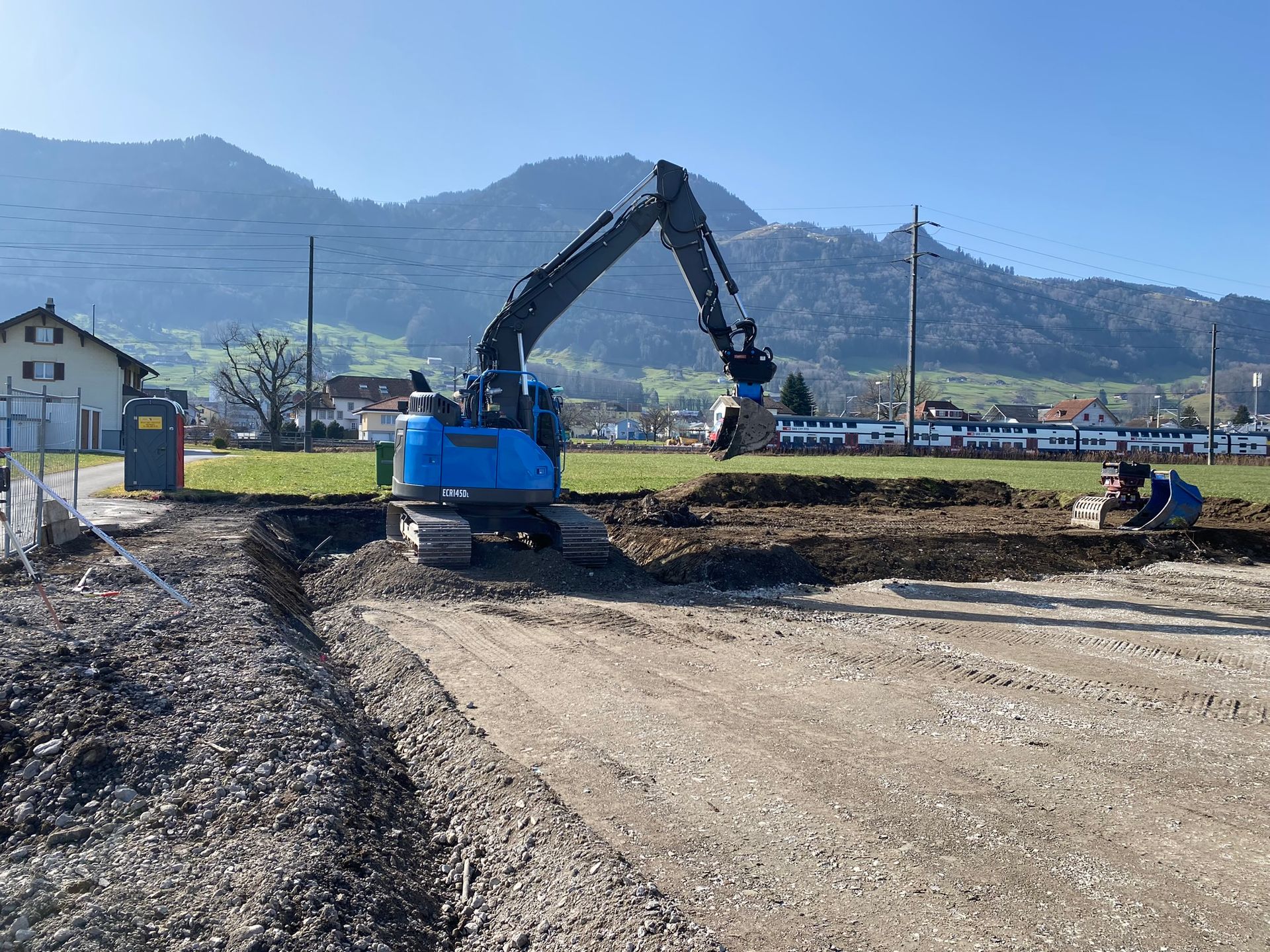 Ein blauer Bagger gräbt ein Loch in ein Erdfeld.