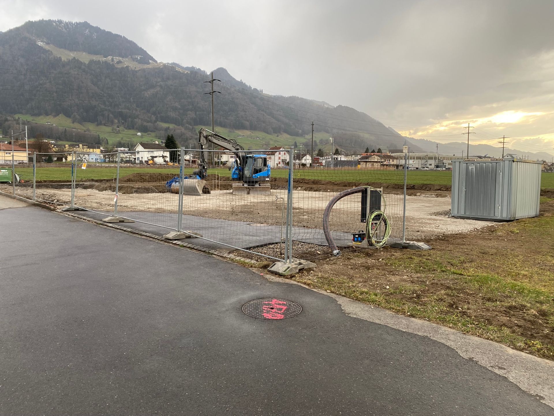 Neben einer Straße entsteht eine Baustelle mit Bergen im Hintergrund.