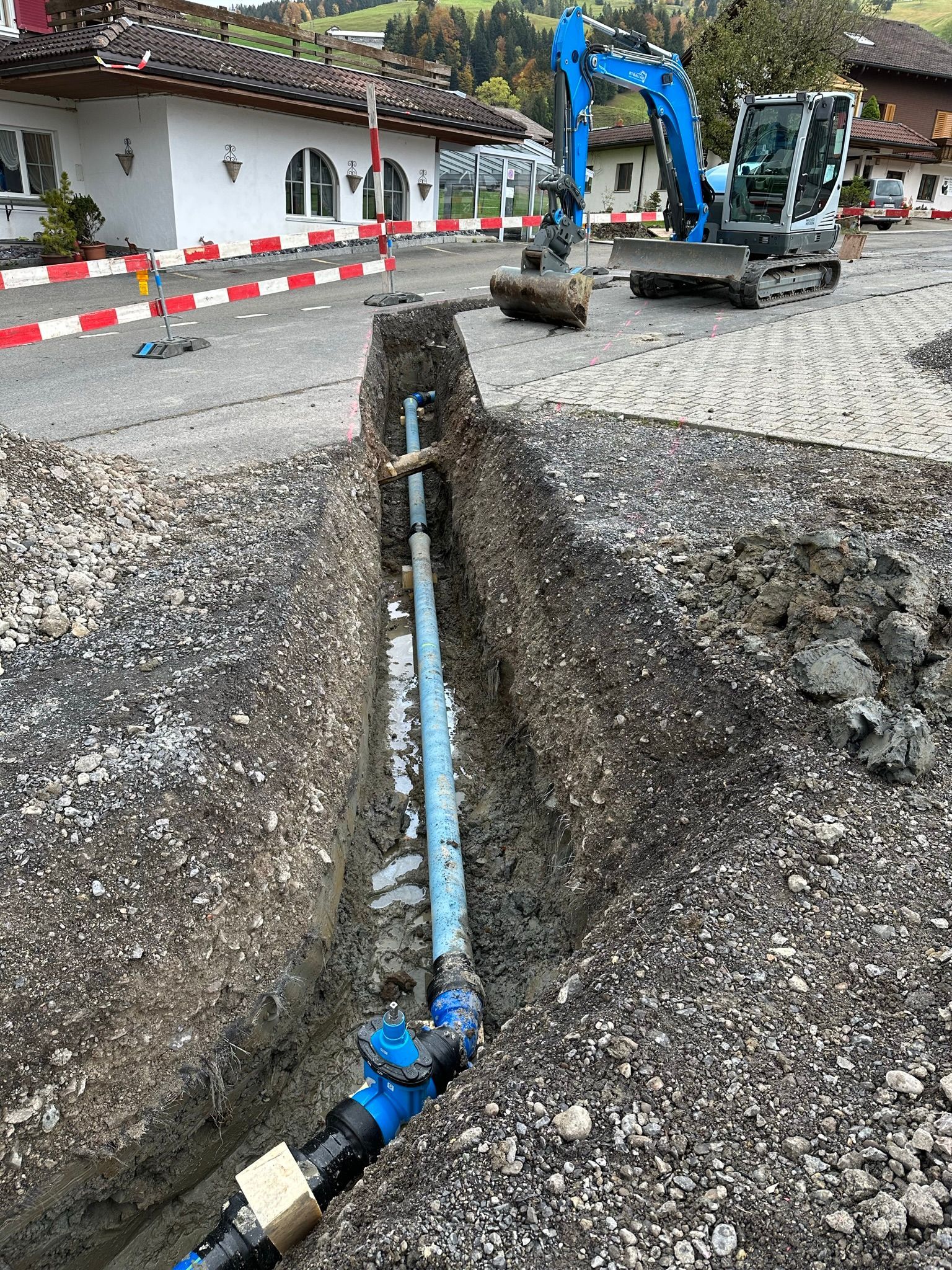 Ein blauer Bagger gräbt neben einem blauen Rohr ein Loch in den Boden.