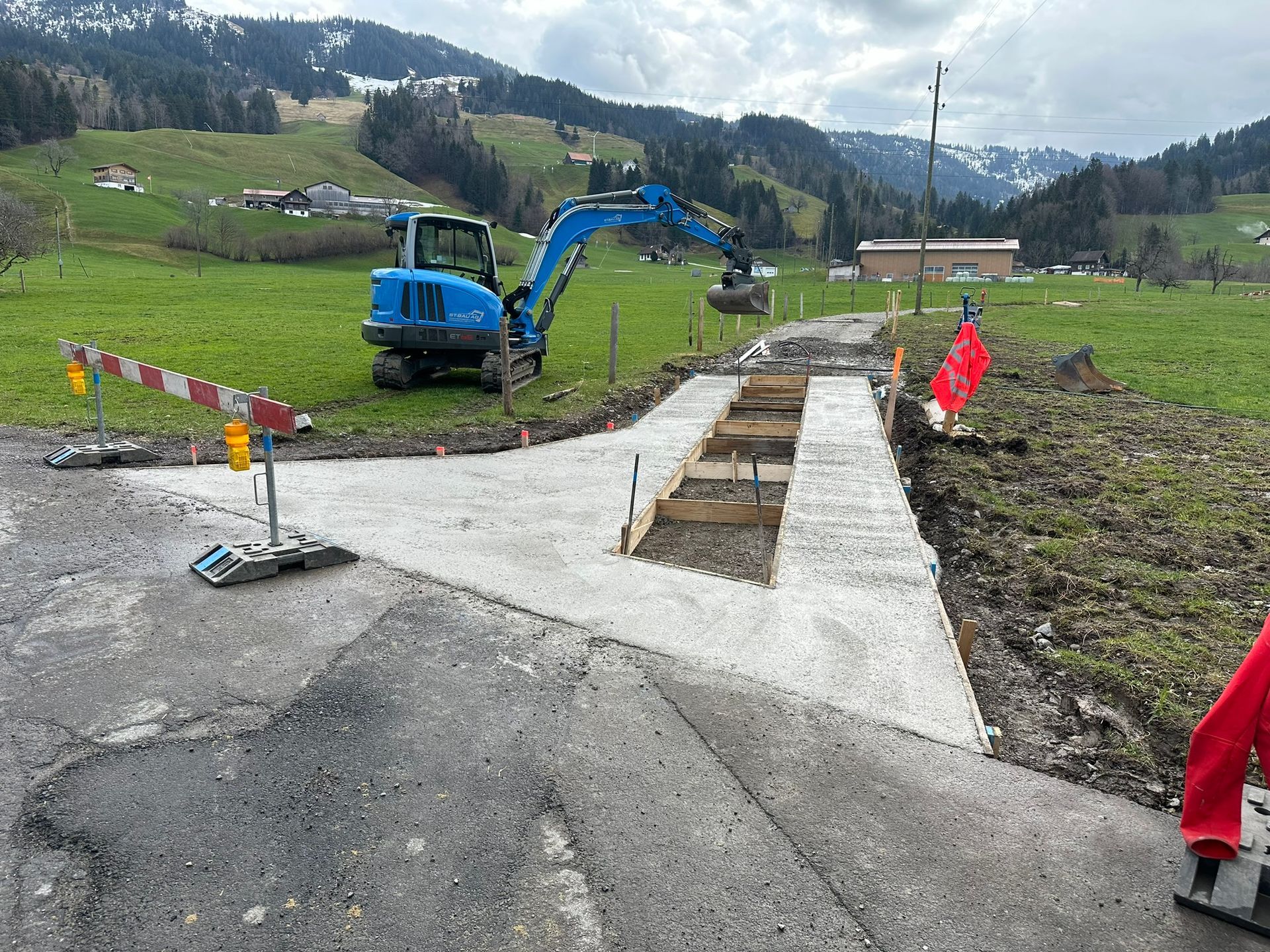 Ein blauer Bagger arbeitet an einer Straße auf einem Feld.