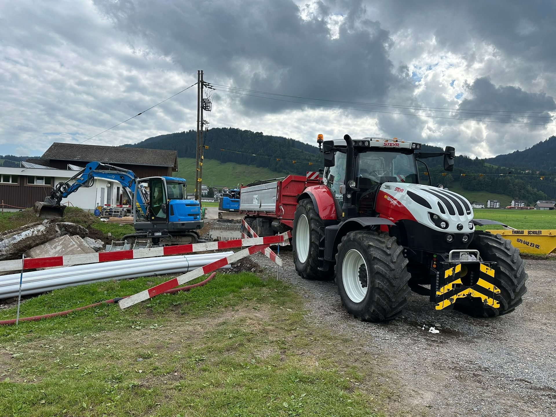 Auf einem Schotterplatz steht ein Traktor mit einem daran befestigten Anhänger.