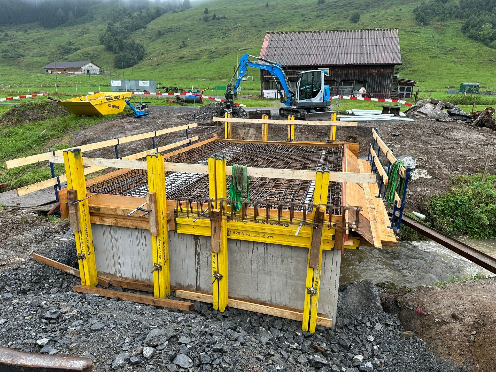 Eine Baustelle mit einem Gebäude im Hintergrund und einem blauen Bagger im Vordergrund.