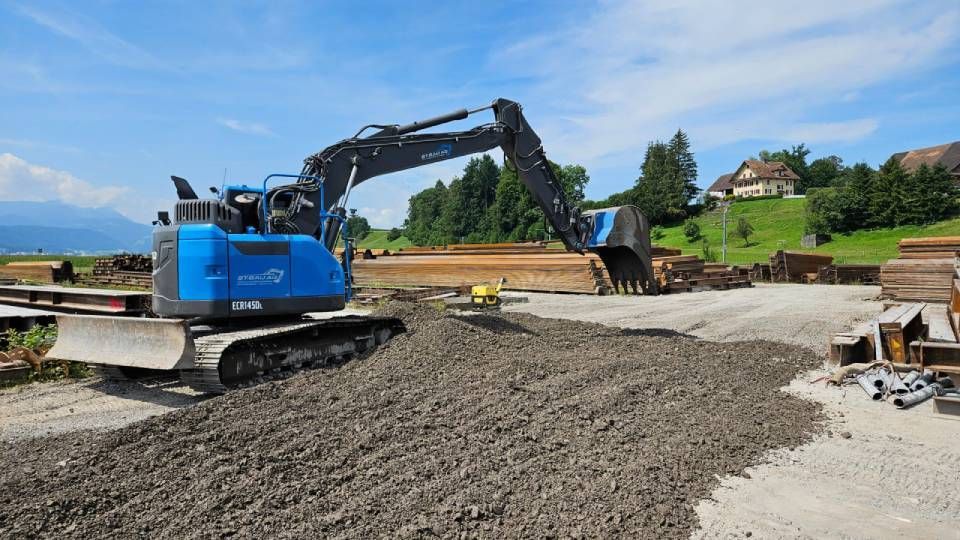 Ein blauer Bagger bewegt Erde auf einer Baustelle. Foto von der ST-Bau AG