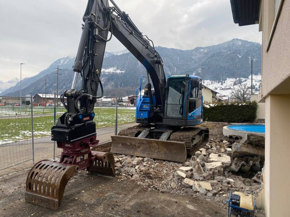 Ein grosser Bagger arbeitet auf einer Baustelle mit Bergen im Hintergrund. Foto von der ST-Bau AG
