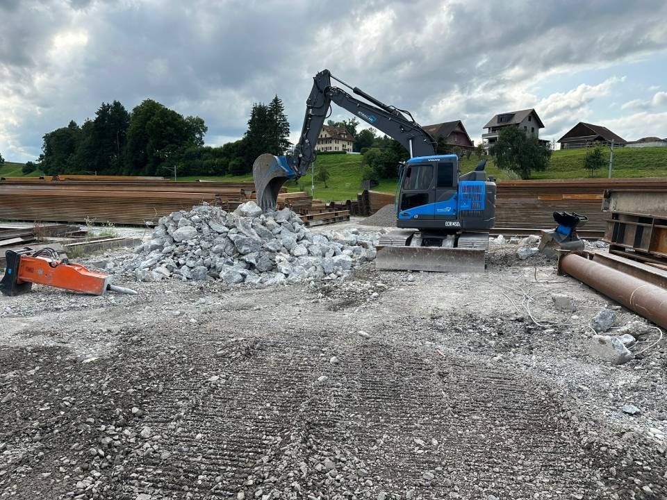 Ein roter Bagger gräbt vor einem Haus ein Loch in den Boden.