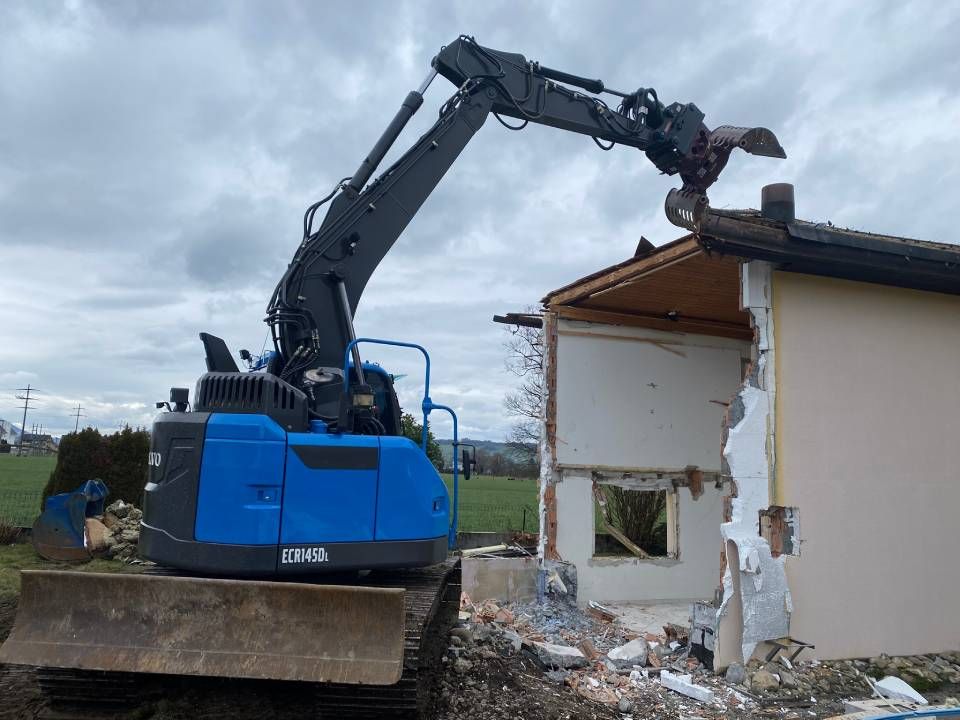 Ein Haus wird mit einem blauen Bagger abgerissen. Foto von der ST-Bau AG