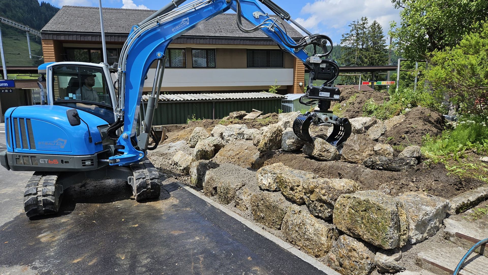 Ein blauer Bagger gräbt vor einem Haus ein Loch.