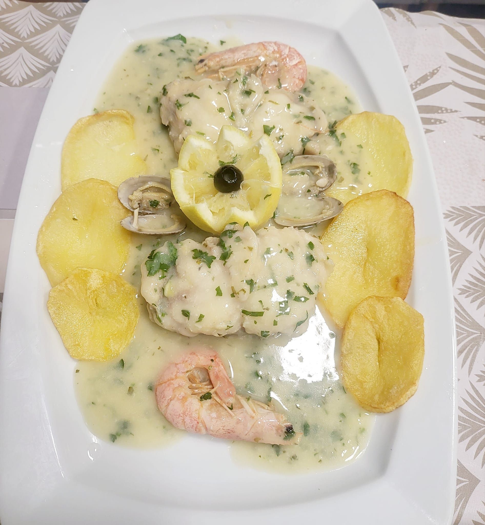 Un plato blanco cubierto con pescado, camarones y patatas sobre una mesa.