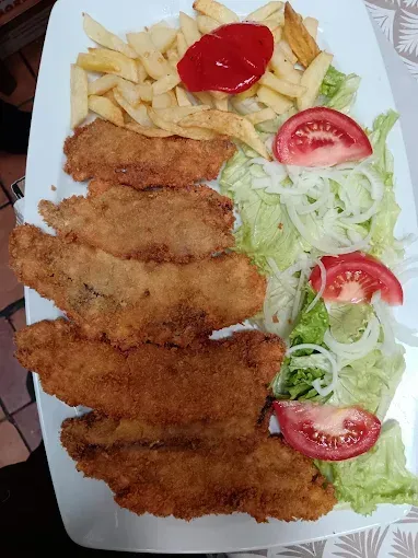 Un plato blanco cubierto con pollo frito, papas fritas, lechuga y tomates.