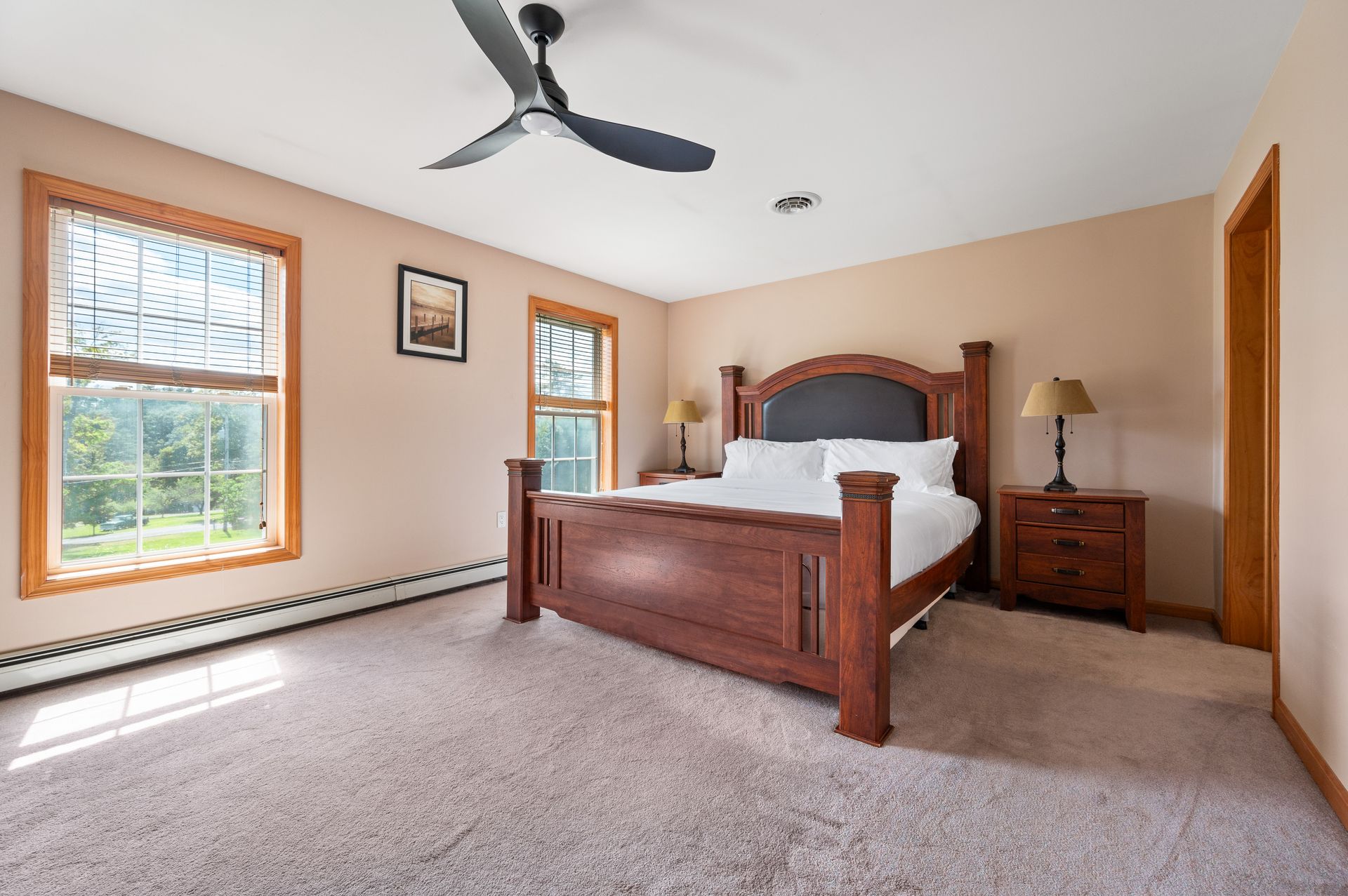 Bedroom with a brown wooden bed, two windows, and beige carpet.