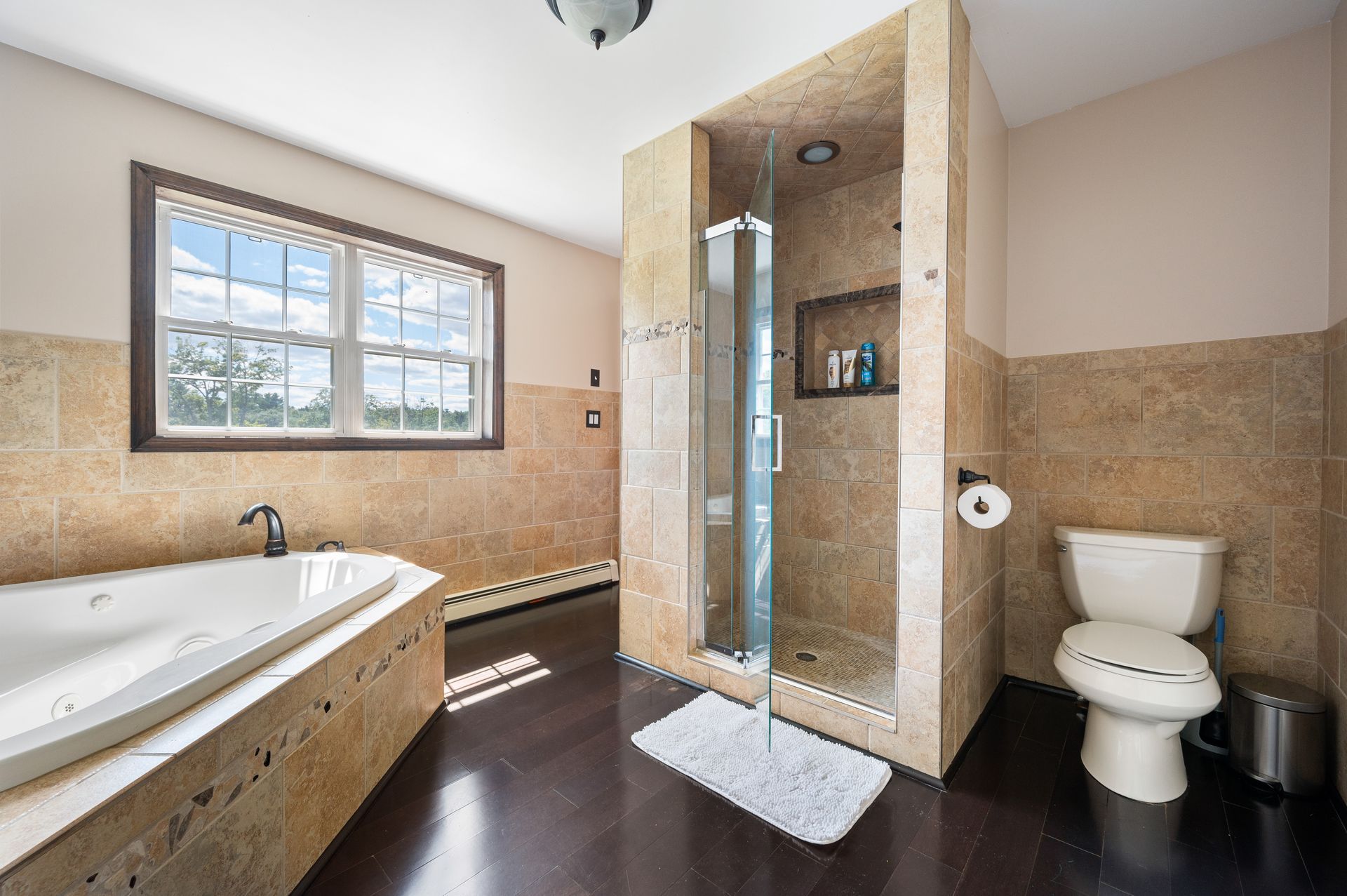 Bathroom with tiled walls, dark wood floor, bathtub, shower, toilet, and window.