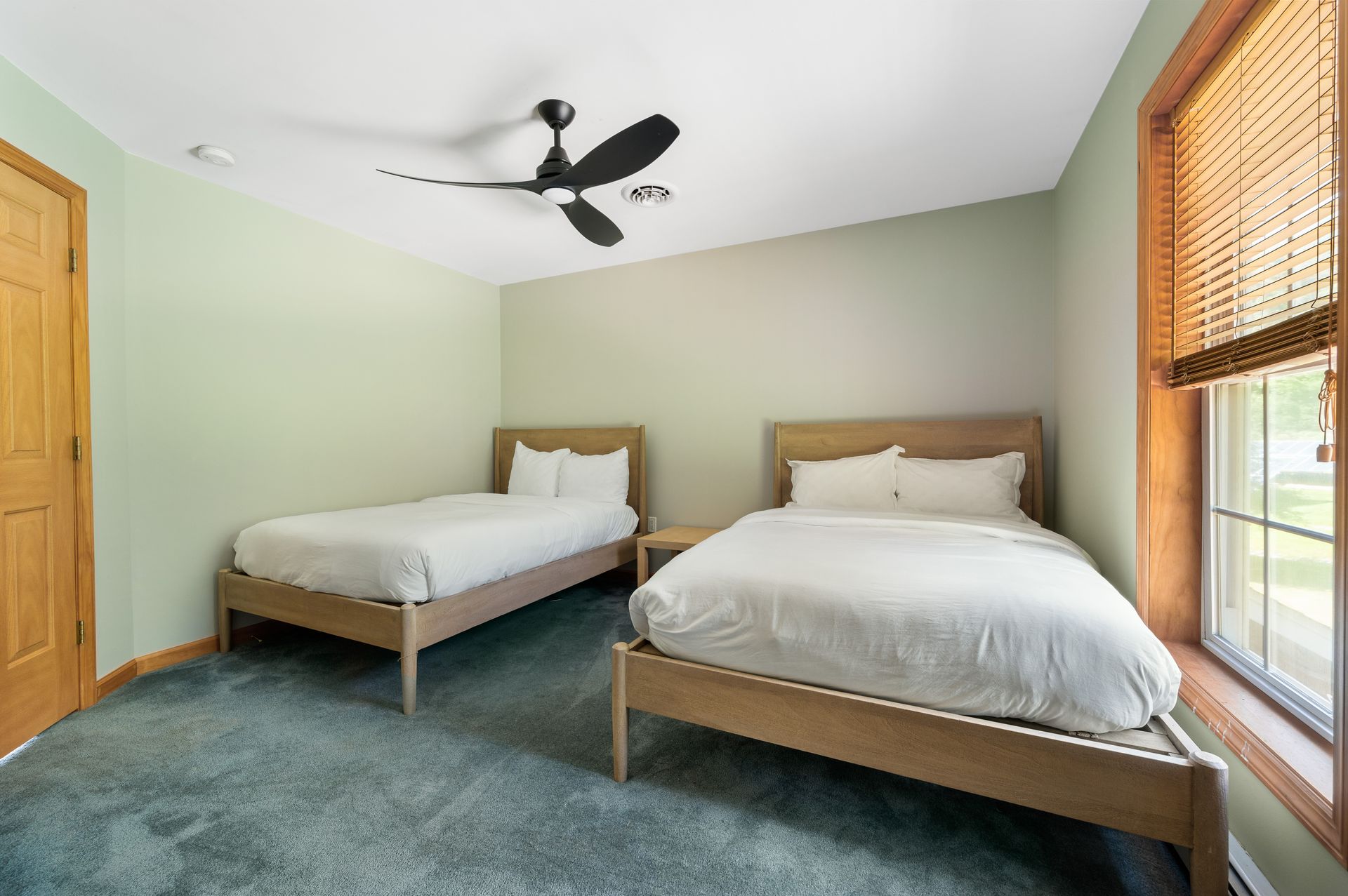 Bedroom with two twin beds, pale green walls, blue carpet, wood door/window trim, and ceiling fan.