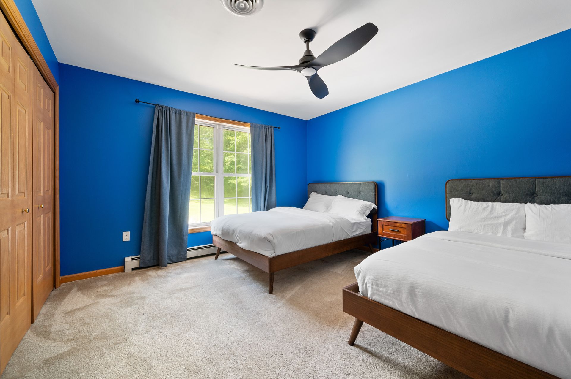 Bedroom with two beds, blue walls, wooden closet, window, and ceiling fan.