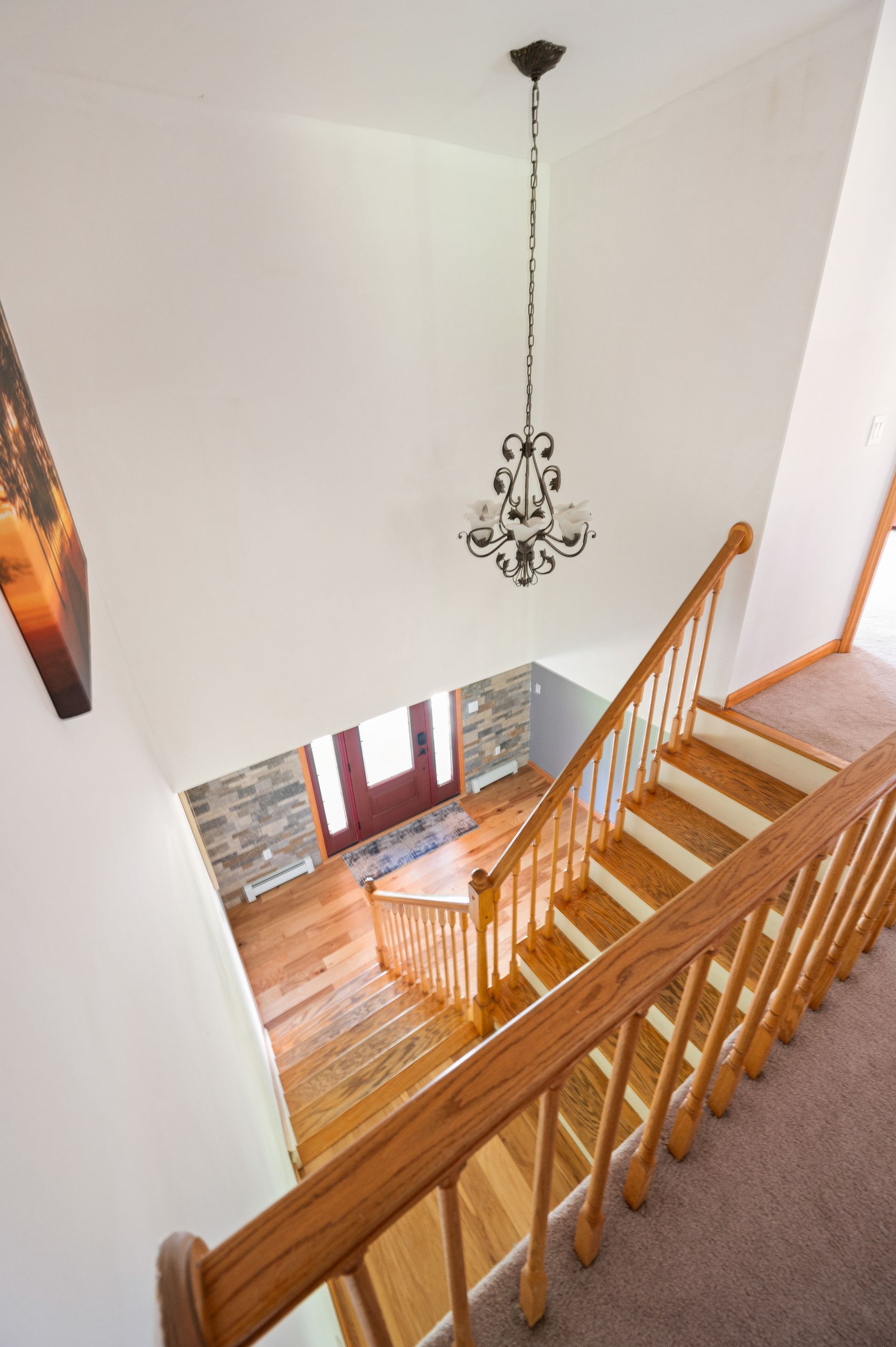 Staircase leading down, viewed from above, with wooden railings, chandelier, and a front door visible.