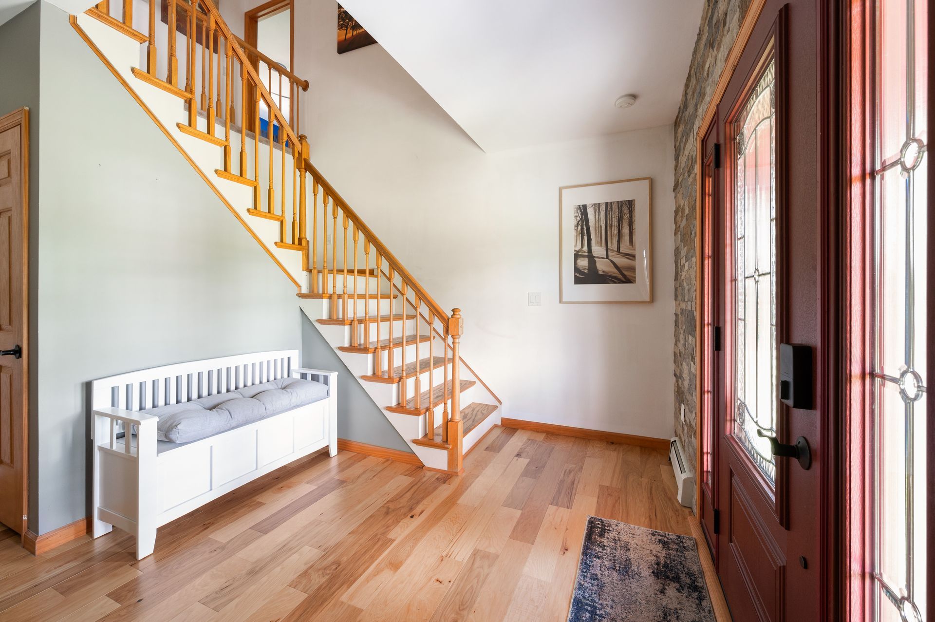 Entryway with wooden staircase, bench, and front door with glass panels.
