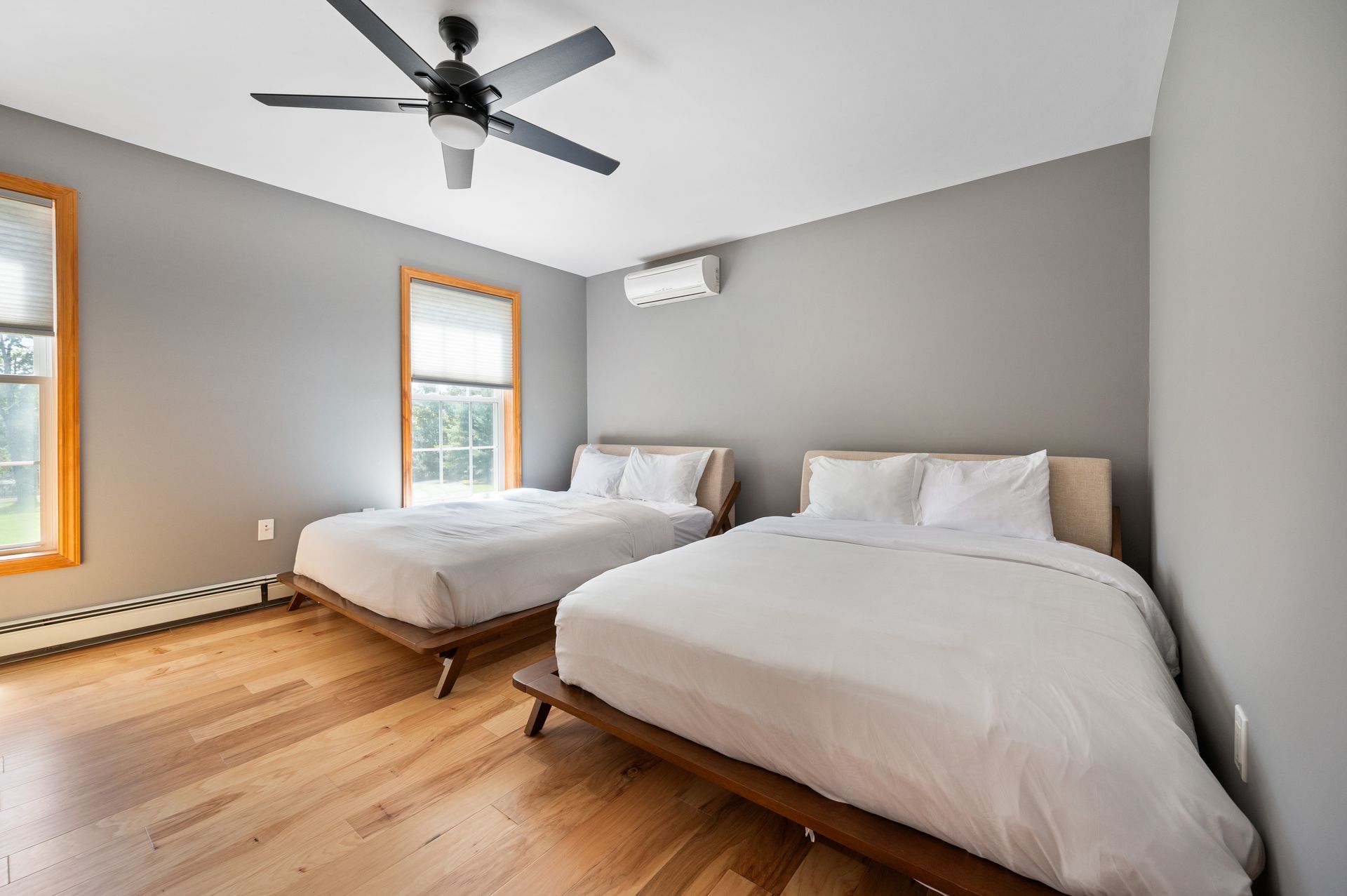 Two beds in a room with gray walls, wooden floor, and a ceiling fan.