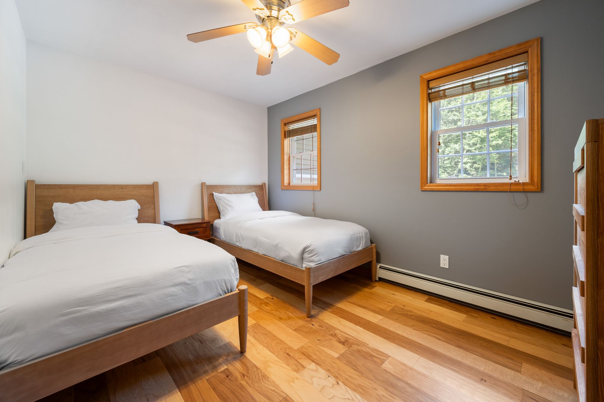 Bedroom with two twin beds, wooden floors, windows with blinds, and ceiling fan.