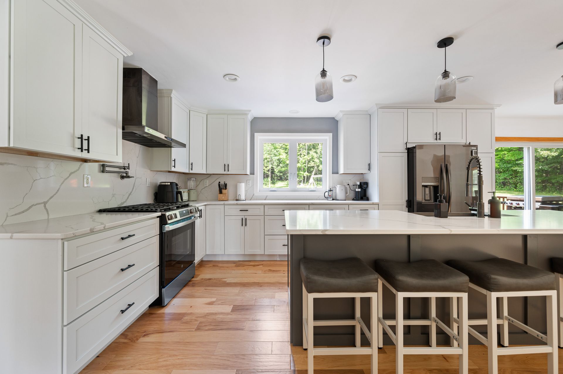 Bright white kitchen with a gray island, stainless steel appliances, and wooden flooring.