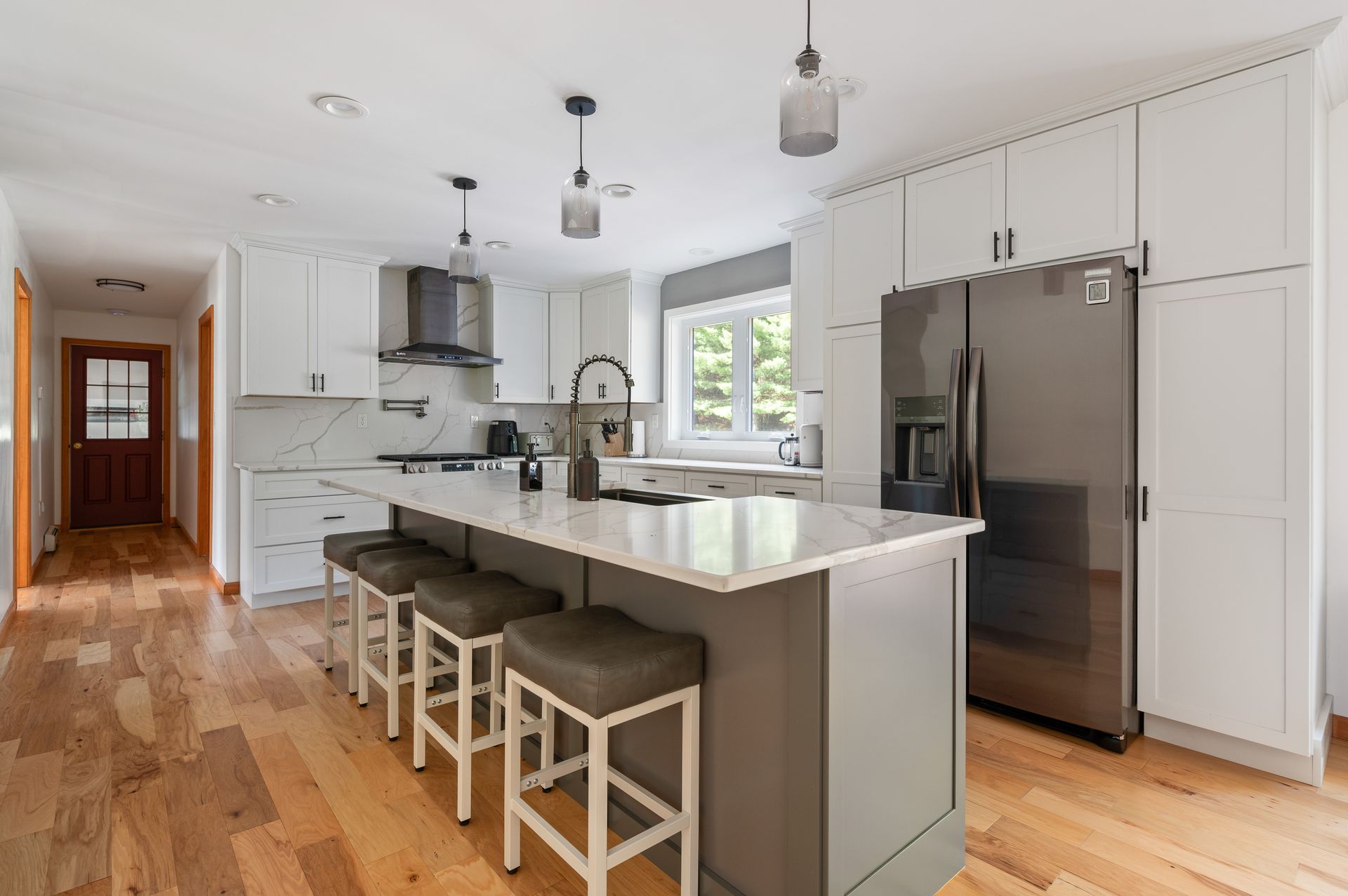 Modern white kitchen with a gray island, stainless steel refrigerator, and wood floor.