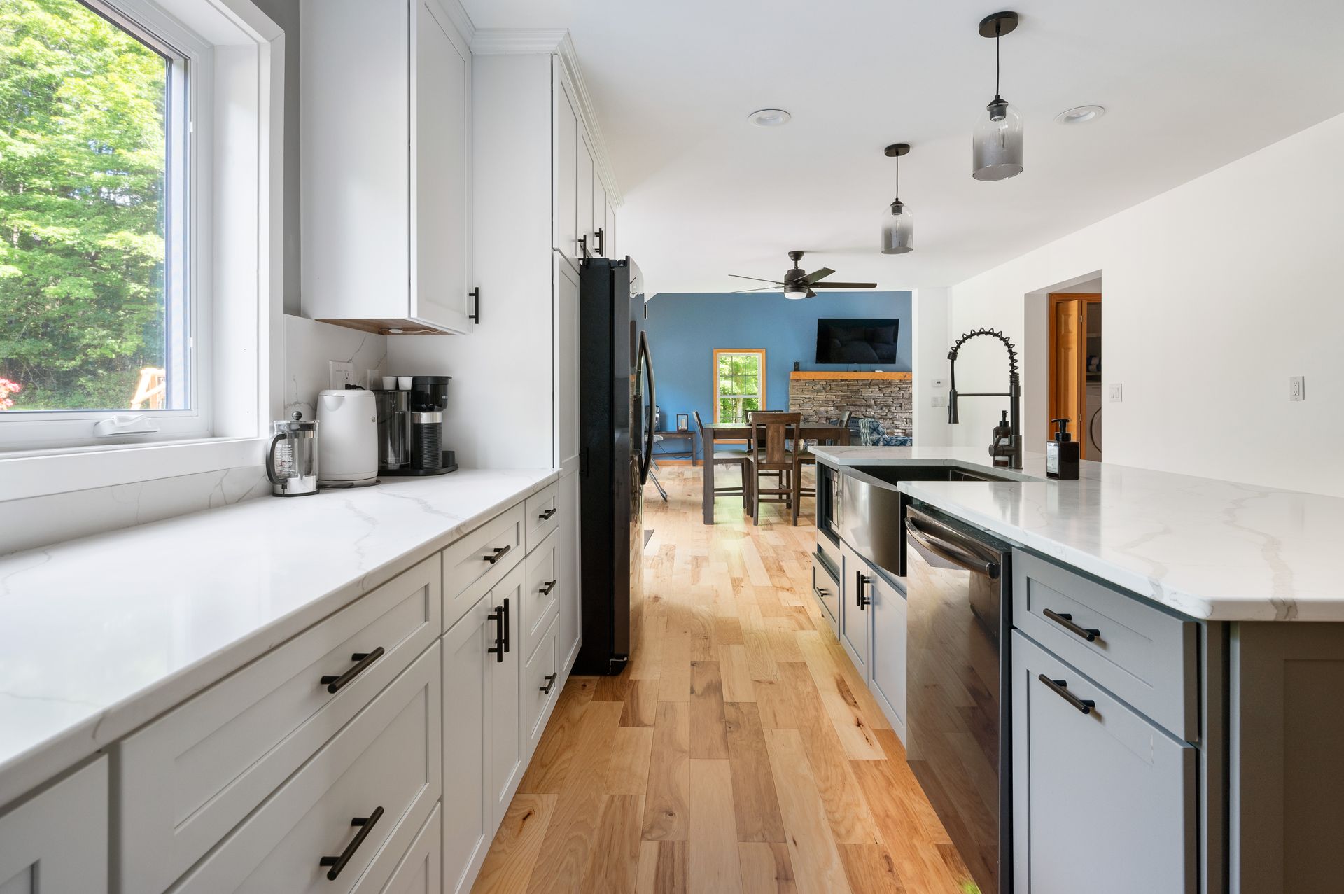 Modern kitchen with white countertops, grey cabinets, and wood floors. Black appliances.