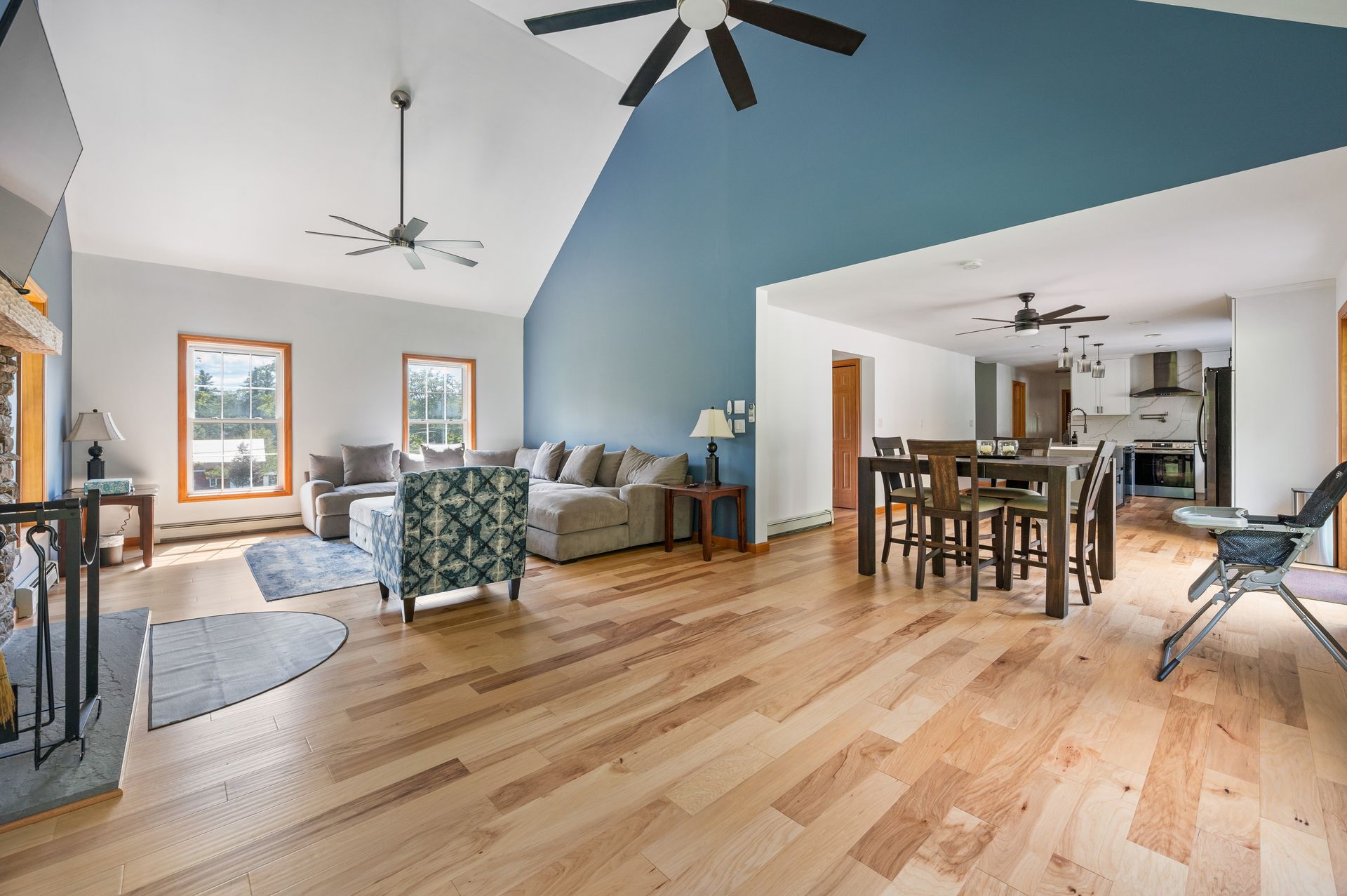 Spacious living room with hardwood floors, vaulted ceiling, and blue accent wall. Dining area and kitchen visible.