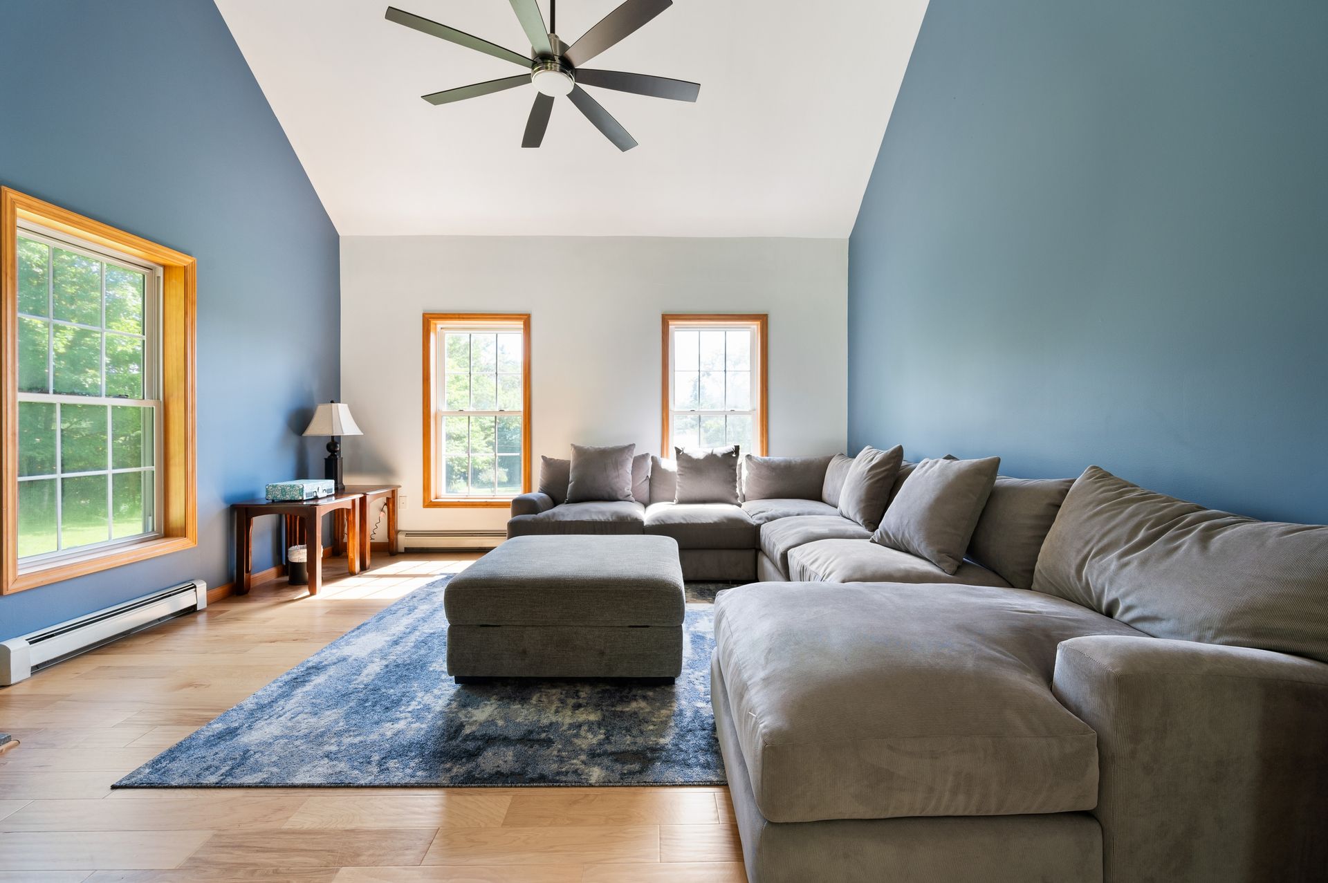 Spacious living room with blue walls, large gray sectional sofa, and wooden floor.