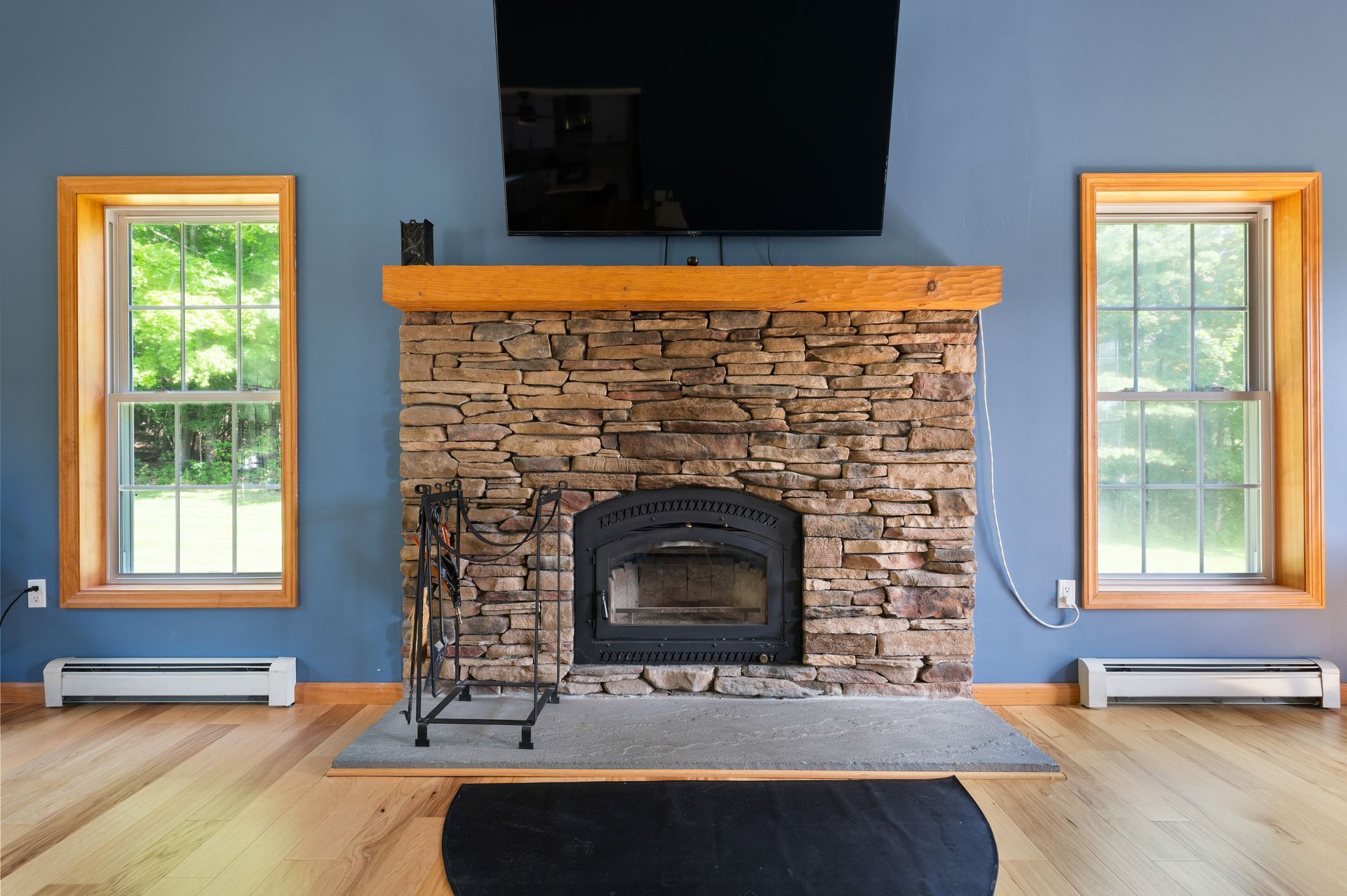 Stone fireplace with mounted TV, flanked by windows with wood trim, on blue wall.