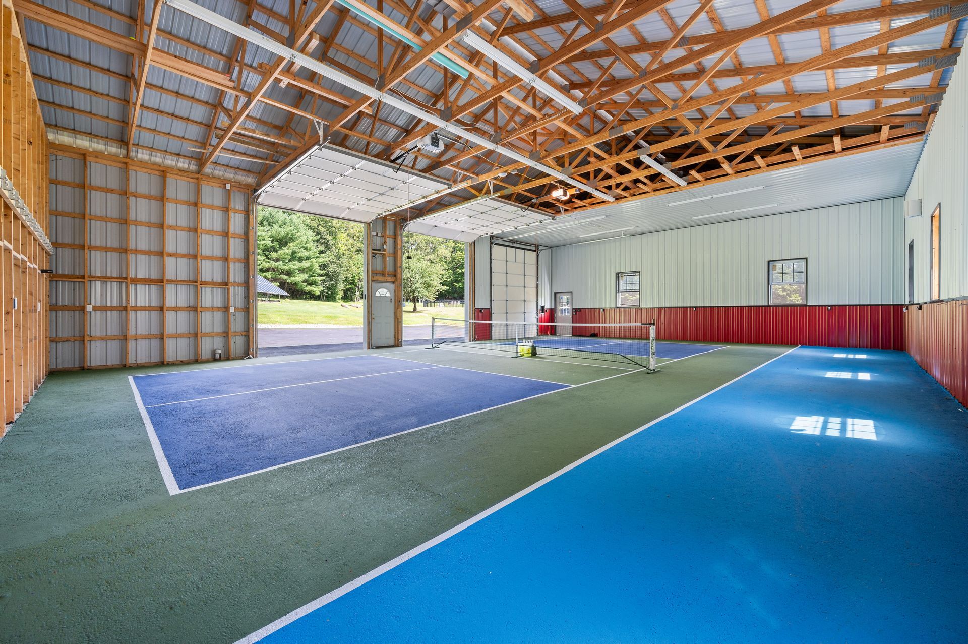 Indoor court with blue and green floor, net, and open garage door to the outdoors.