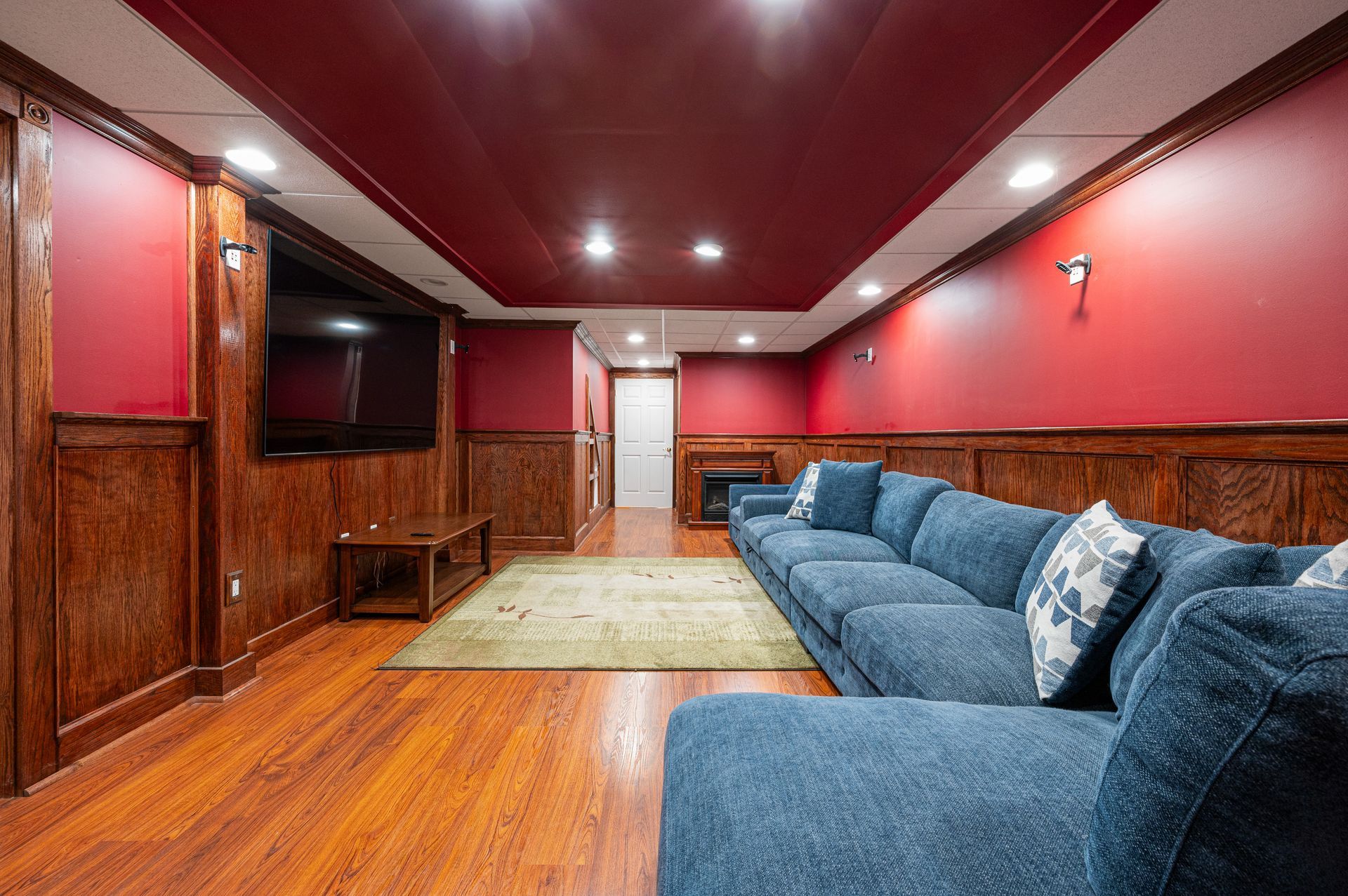 Living room with red walls, wood paneling, blue sectional sofa, and a large TV.