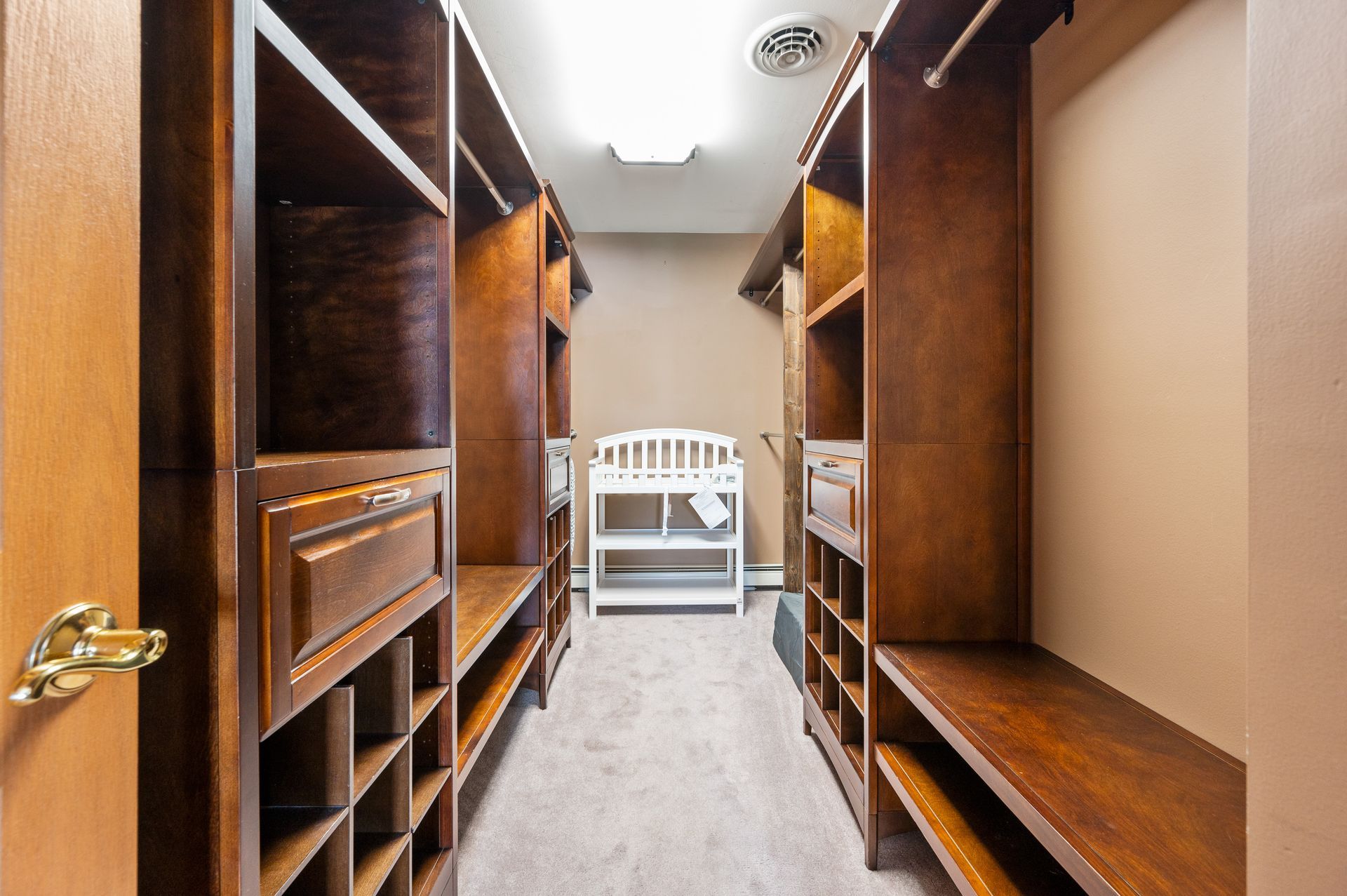 A walk-in closet with dark wood shelving and storage, a baby changing station, and a rug.