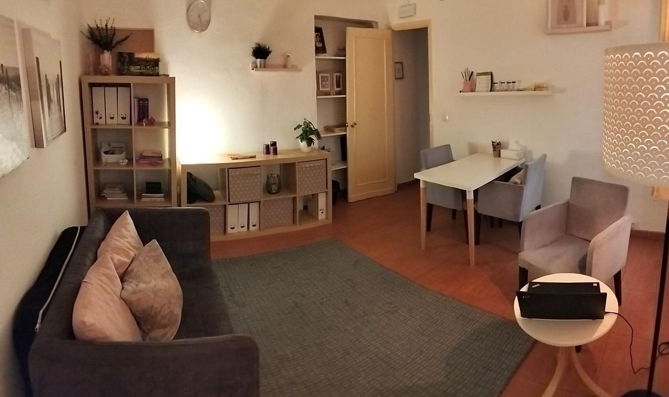 Una sala de estar con un sofá gris, una estantería baja de madera, una mesa de comedor con dos sillas y una lámpara de pie.