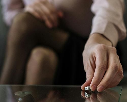 Una mano coloca un anillo de bodas sobre una mesa de cristal.