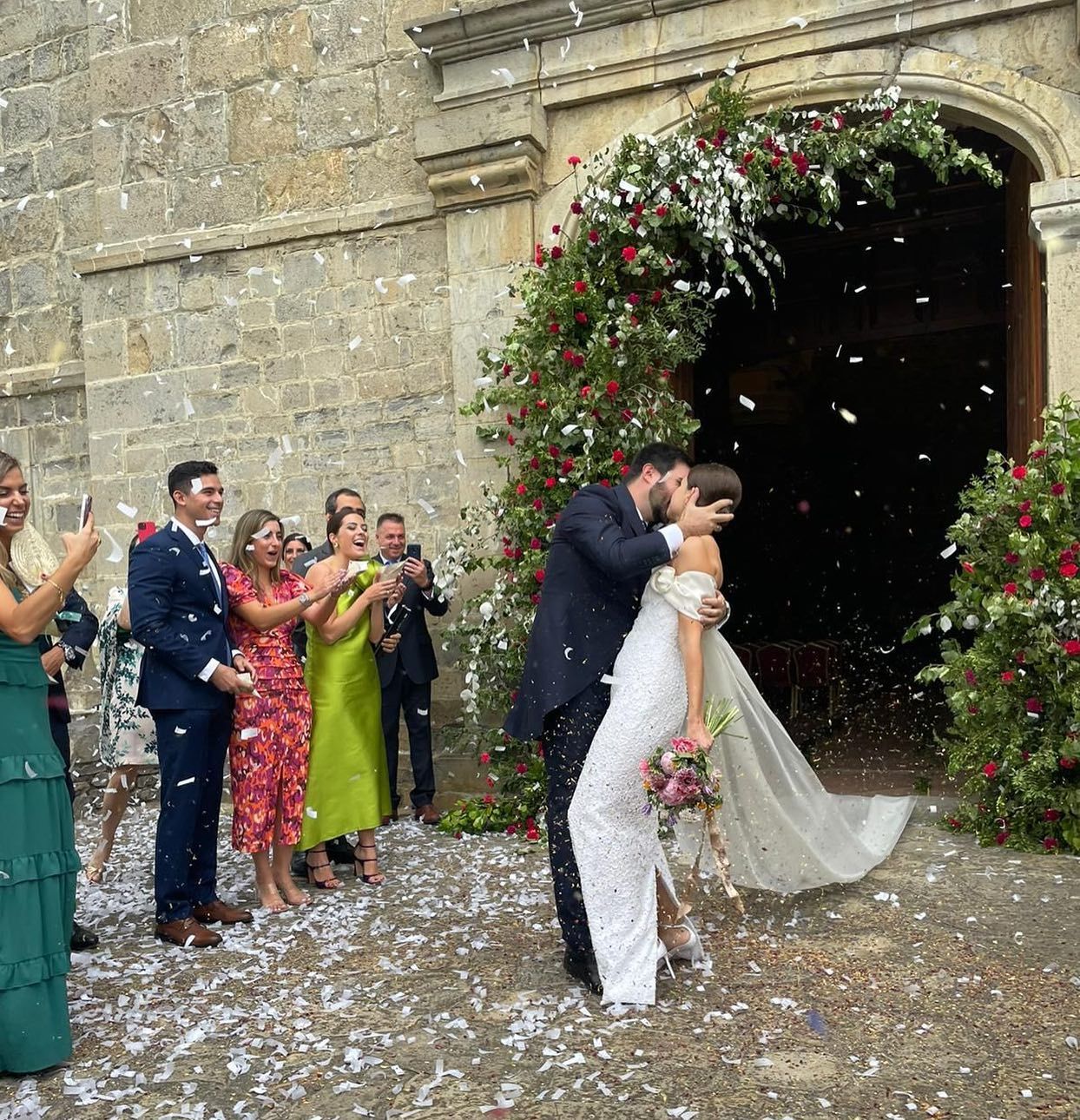 Una novia y un novio besándose delante de una multitud de personas.