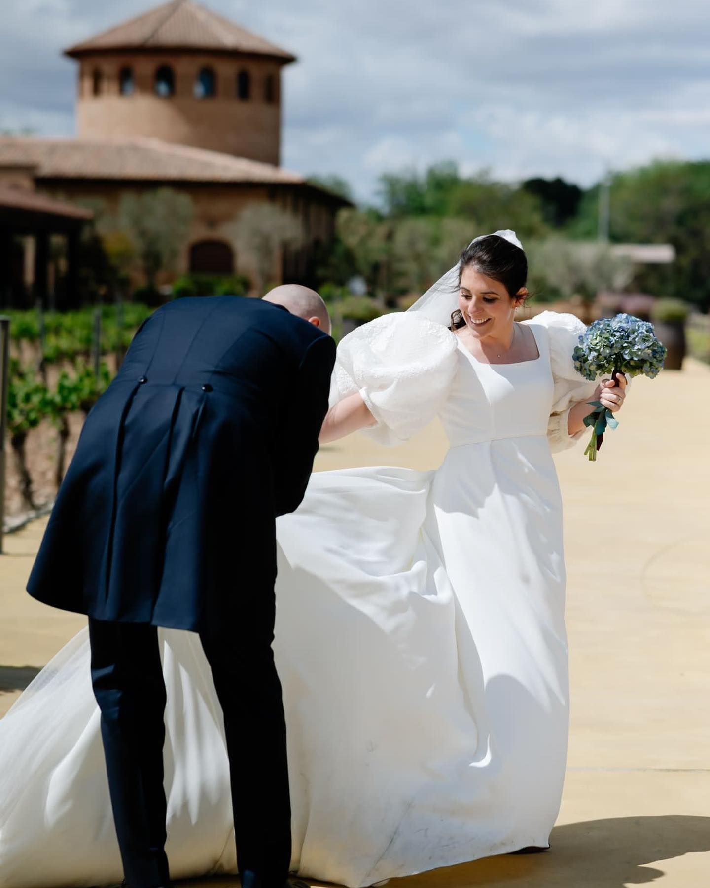 Una novia con un vestido blanco está siendo ayudada por su novio.