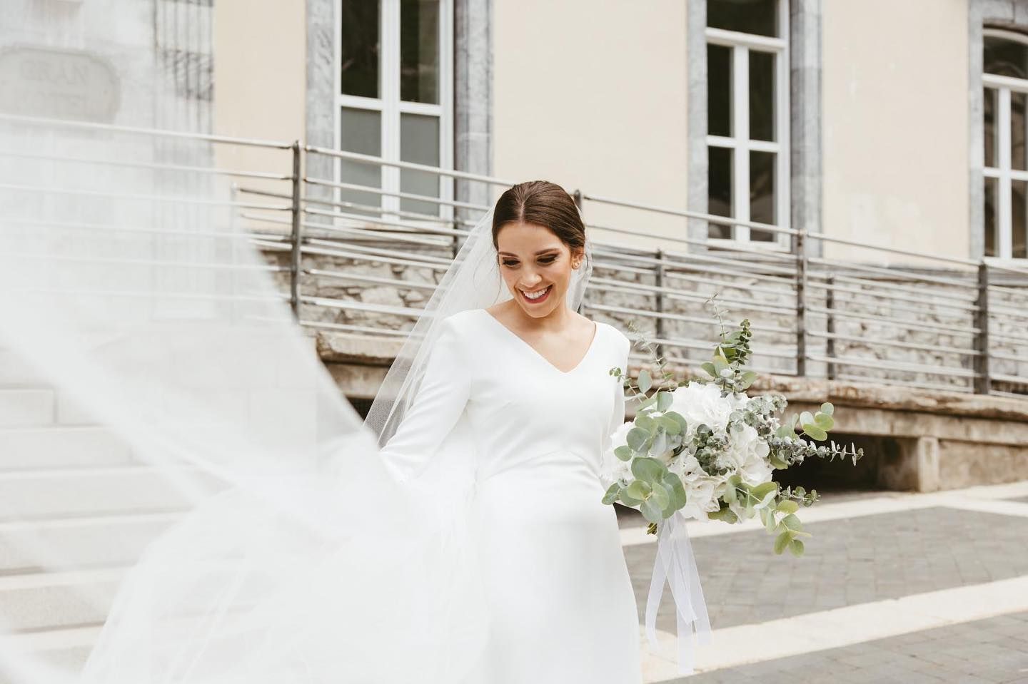 Una novia con un vestido blanco y velo sostiene un ramo de flores.