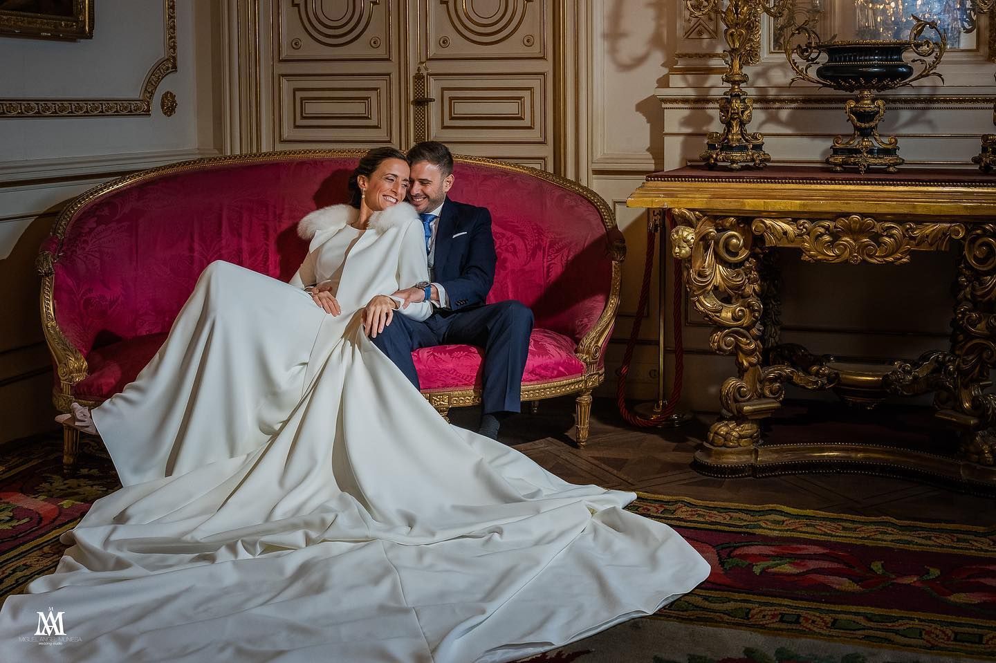 Una novia y un novio están sentados en un sofá rojo.