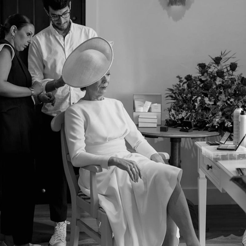 Una mujer con un vestido blanco está sentada en una silla mientras un hombre le seca el cabello.