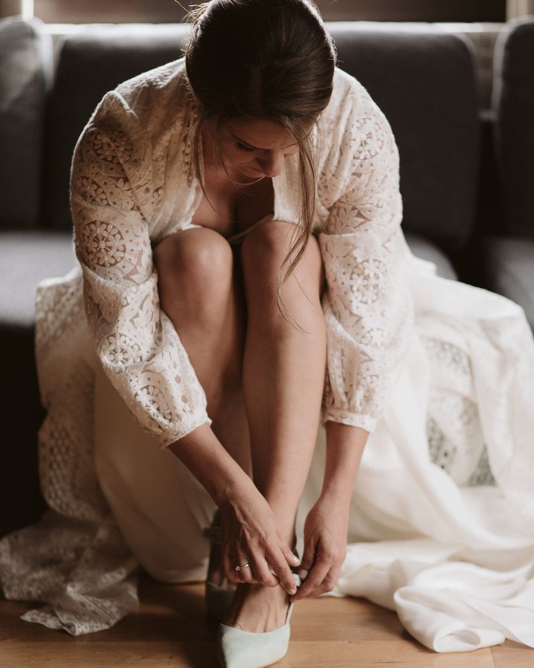 Una mujer con un vestido de novia está sentada en el suelo atándose los zapatos.