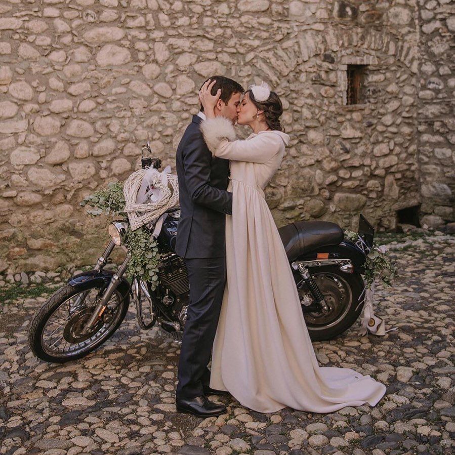 Una novia y un novio se besan delante de una motocicleta.