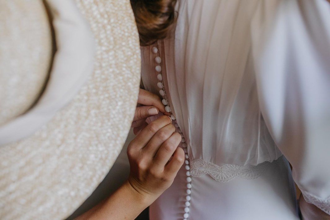 Una mujer está ayudando a otra mujer a abrocharse el vestido de novia.