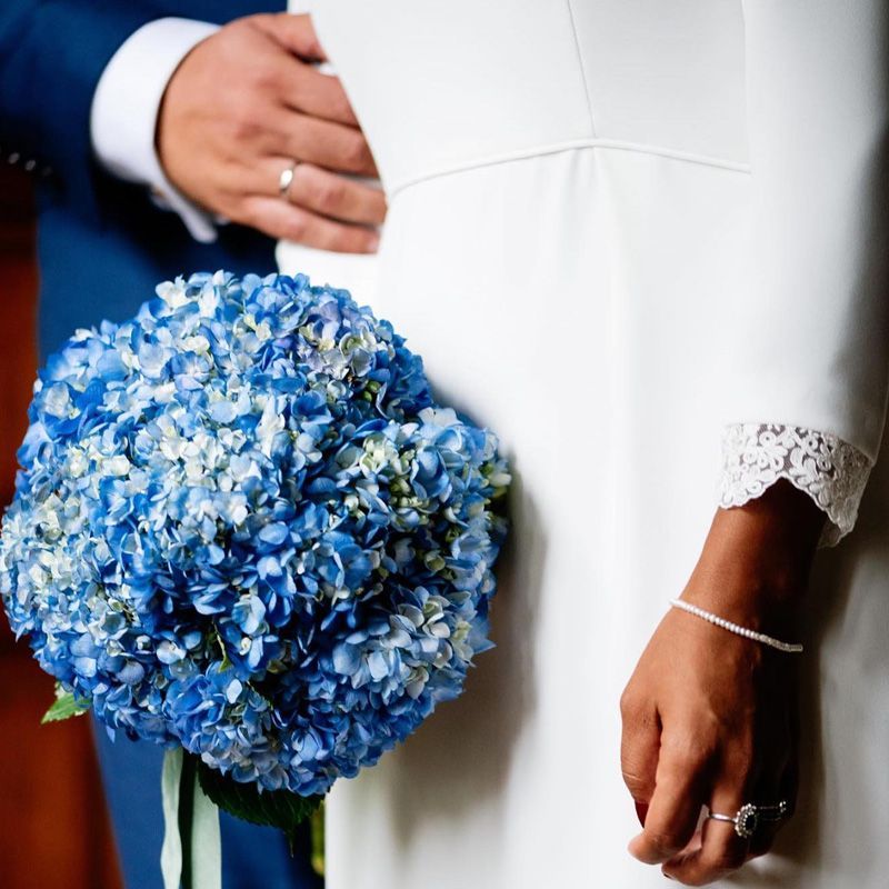 Una novia con un vestido blanco sostiene un ramo de flores azules.