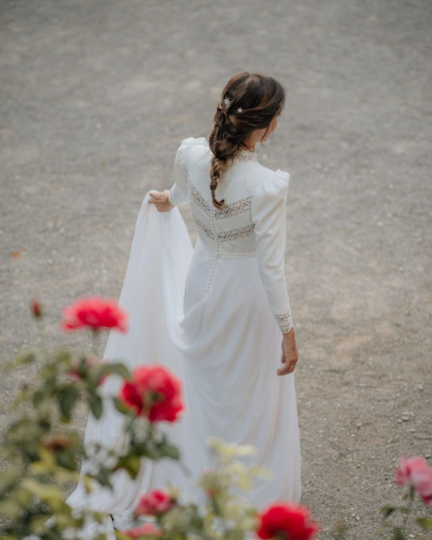 Una mujer con un vestido blanco está parada delante de rosas rojas.