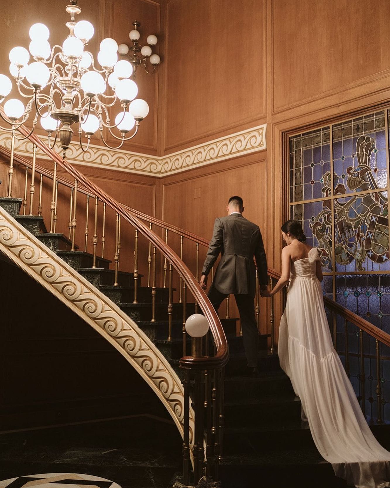 Una novia y un novio bajan una escalera de caracol tomados de la mano.
