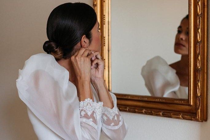 Una mujer con un vestido blanco se mira reflejada en un espejo.