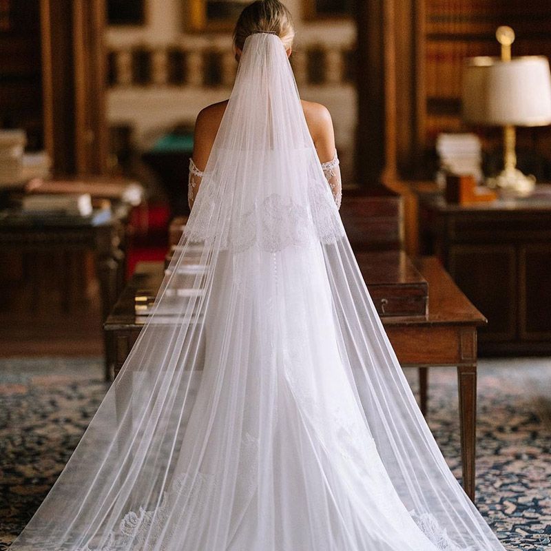 Una novia con un vestido de novia blanco y velo está de pie frente a una mesa.