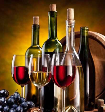 Un montón de botellas de vino y copas con uvas al fondo.