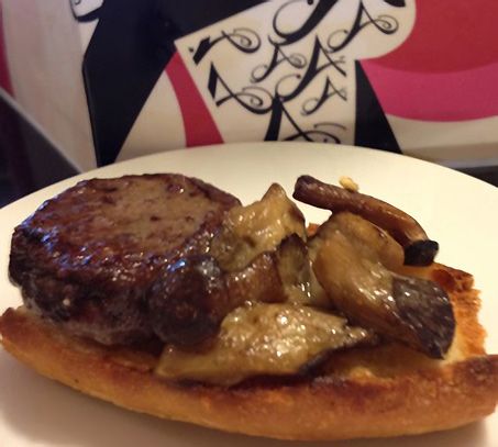 Un plato blanco con una hamburguesa y champiñones encima.