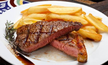 Un plato blanco cubierto con un filete y papas fritas.